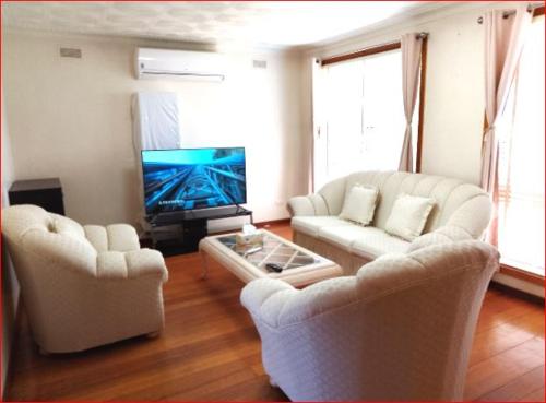 a living room with two white couches and a tv at Charming Three-Bedroom Holiday Home Near Tourist Attractions in Werribee