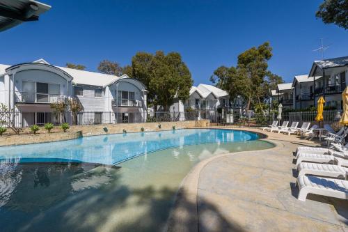 a large swimming pool with white chairs and houses at Mandurah Quay Resort in Mandurah