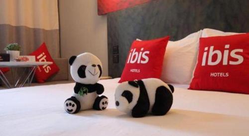 two pandas sitting on a bed with red and white pillows at Ibis Ya An Langqiao in Ya'an