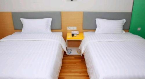 a room with two beds and a night stand between them at 7 Days Inn·Ulanqab Tsining railway station in Ulanqab