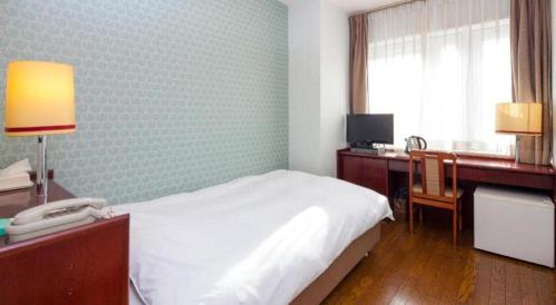 a bedroom with a bed and a desk with a phone at Fukuyama Terminal Hotel in Onomichi