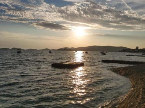 Una puesta de sol sobre un cuerpo de agua con barcos. en Modern Beachfront Apartments near Šibenik, en Srima