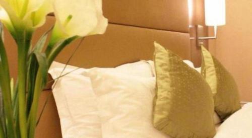 a bed with pillows and a vase with a flower at Jiaxin Conifer Hotel Shunde in Shunde