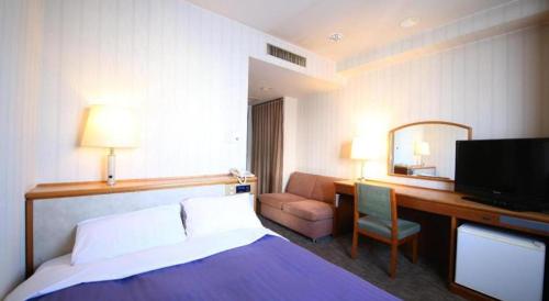 a hotel room with a bed and a desk with a television at Centia Hotel Naito in Kofu