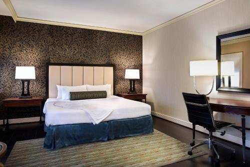 a hotel room with a bed, chair, desk and a lamp at The Whitehall Houston in Houston