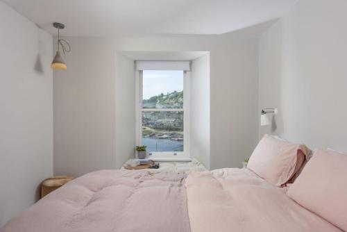 a white bedroom with a large bed and a window at Berlewen, Mousehole in Mousehole