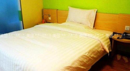 a bedroom with a white bed with a green wall at 7 Days Inn Hami Baofeng Market in Qumul