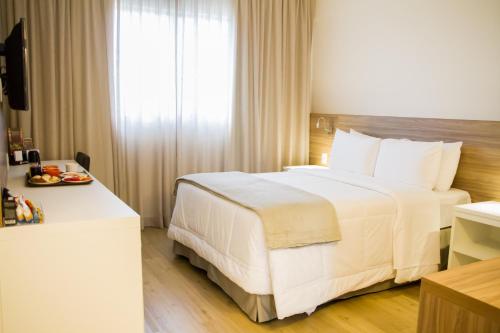 a hotel room with a large white bed and a window at Intercity Gravataí in Gravataí
