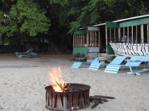 a fire pit on a beach with chairs and a building at Norman Carr Cottage in Monkey Bay
