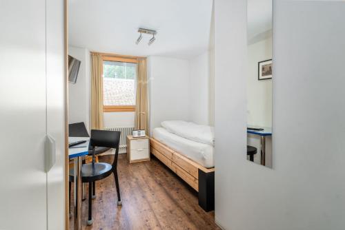 オーバーヴァルトにあるHotel Furkaのベッド、デスク、デスクが備わる小さな客室です。