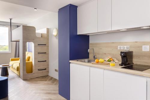 une cuisine avec des armoires blanches et un mur bleu dans l'établissement Appart'City Collection Paris Roissy CDG Airport, à Roissy-en-France
