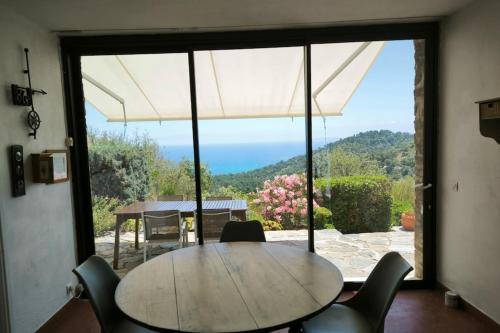 une table et des chaises dans une pièce avec une grande fenêtre dans l'établissement Atypical house with garden in Bormes-les-Mimosas, à Bormes-les-Mimosas