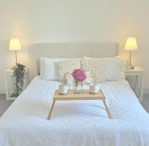 a bed with a table with two cups and flowers on it at Fig Tree Cottage in North Cornelly