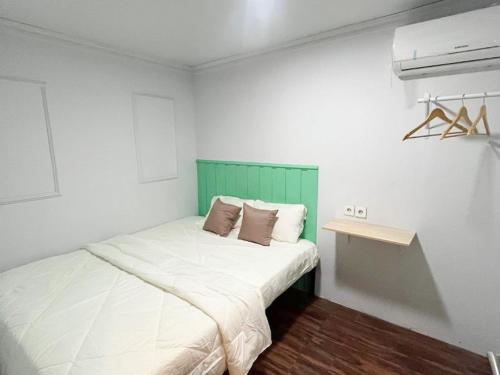 a white bedroom with a bed with a green headboard at RedDoorz Syariah at Budget Guesthouse Sepaku in Sepaku