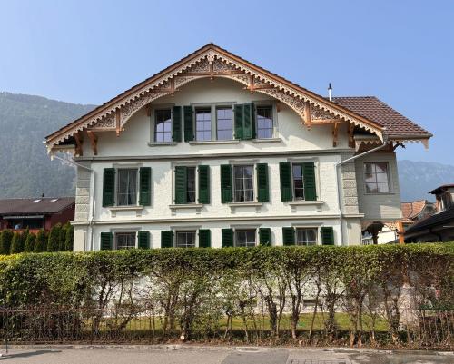 une grande maison blanche avec des fenêtres vertes à volets dans l'établissement Villa Epoka, à Interlaken