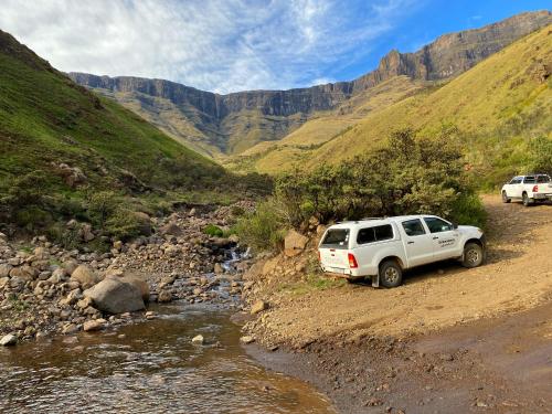two cars parked on a dirt road next to a river at Sani Lodge & Cottages in Sani Pass