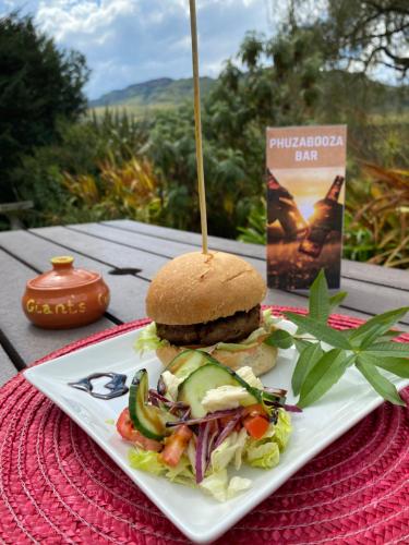a sandwich on a plate on a table with a book at Sani Lodge & Cottages in Sani Pass