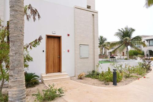 a white house with a wooden door next to a palm tree at استيديو هوانا صلاله Hawana Salalah studio in Wādī Khasbar