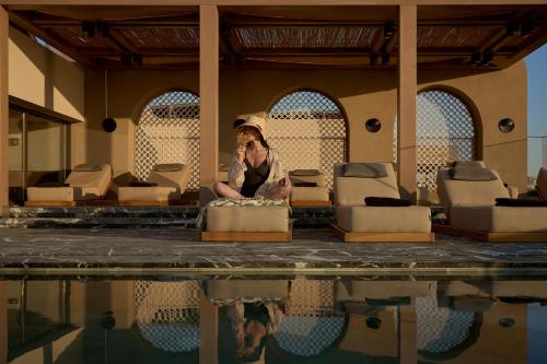 a woman sitting in a chair next to a pool at Rocca a Mare Heraklion - Handwritten Collection in Heraklio Town