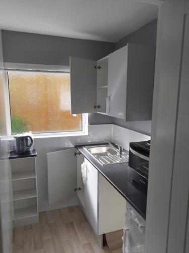 a kitchen with white cabinets and a sink and a window at Studio Twenty One in Whitburn