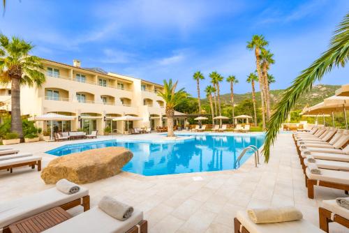 a resort pool with chaise lounge chairs and palm trees at Hotel Corsica & Spa Serena in Calvi