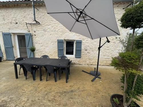 a table with chairs and an umbrella in front of a building at Maison à la campagne in Massels
