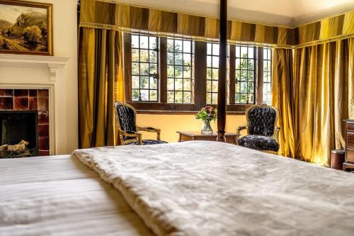 a bedroom with a large bed with two chairs and a fireplace at Caer Beris Hotel in Builth Wells