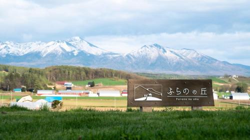 a sign in a field with mountains in the background at ふらのの丘 in Kami-furano