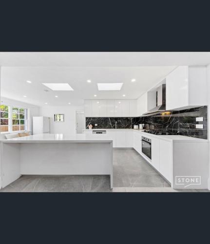 a kitchen with white cabinets and black counter tops at Spacious 5BD Garden House in Hornsby close 2 train in Hornsby