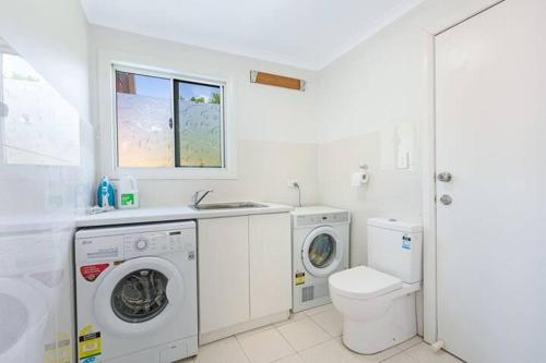 a white bathroom with a washing machine and a toilet at Spacious 5BD Garden House in Hornsby close 2 train in Hornsby