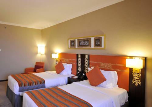 a hotel room with two beds and a chair at Millennium Taiba Hotel in Al Madinah