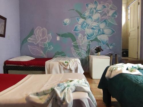 a room with two beds and a mural of flowers at Pousada Dádiva Encanto da Orquídea Praia do Pontal Centro in Paraty