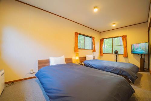 two beds in a room with yellow walls and windows at クラレンス-森の中でBBQと4Kプロジェクターが楽しめる北軽井沢の貸切Villa- in Kita-karuizawa