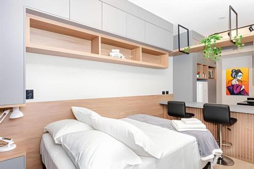 a bedroom with a white bed and a kitchen at Sky Batel - Apartamentos UROOMS in Curitiba
