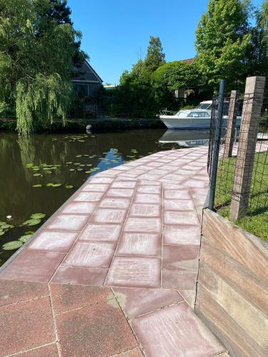 a brick walkway next to a river with a boat at hûske twa in Oudwoude