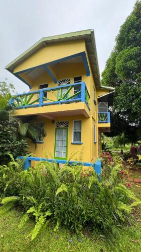 a yellow house with blue balconies in a garden at Jacoway Inn in Calibishie