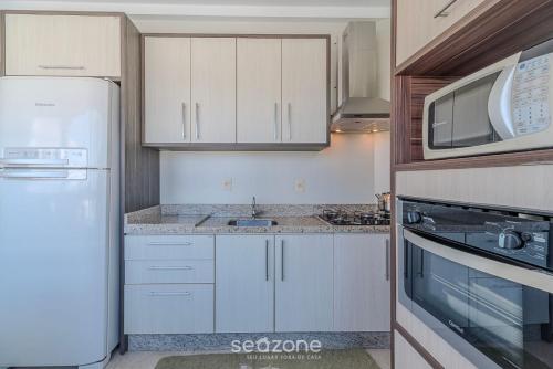 a kitchen with a white refrigerator and a microwave at Apto Charmoso a 550m da Praia Perequê - RNE0301 in Perequê