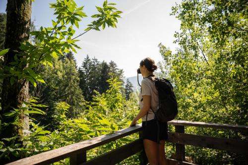 a woman with a backpack standing on a fence in a forest at Hotel Resmairhof in Schenna
