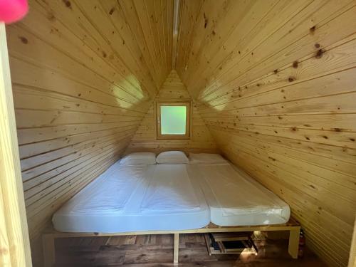 a mattress bed in a wooden cabin with a window at Glamping - domačija Lamperček in Velenje