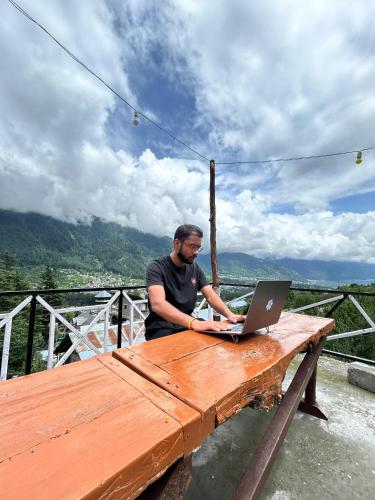 a man sitting at a wooden table with a laptop at The essence of mountains - מהות ההרים in Manāli