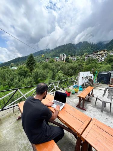 a man sitting at a picnic table with a laptop at The essence of mountains - מהות ההרים in Manāli