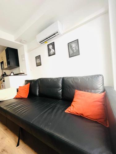 a black leather couch in a living room with orange pillows at Le studio Béthunois - Appart hôtel centre climatisé - All confort in Béthune