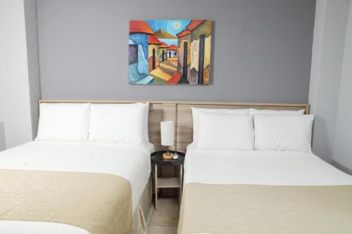 two beds in a room with a painting on the wall at Hotel Los Altos Express "La Centroamerica" in Managua