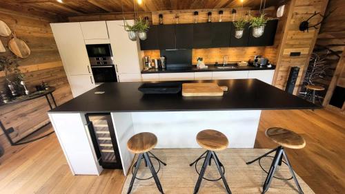 une cuisine avec un comptoir noir et trois tabourets dans l'établissement Résidence PremiÈre Loge - Magnifique chalet, prestations de qualité, bel emplacement MAE-3371, aux Gets