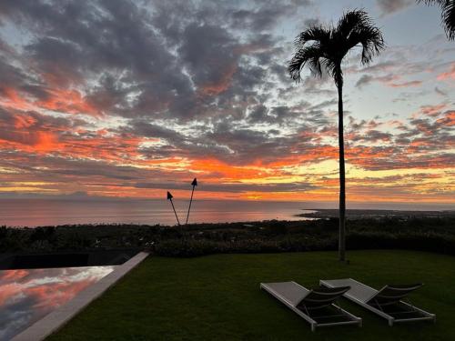 a sunset with two lounge chairs and a palm tree at Hale La'i in Kailua-Kona