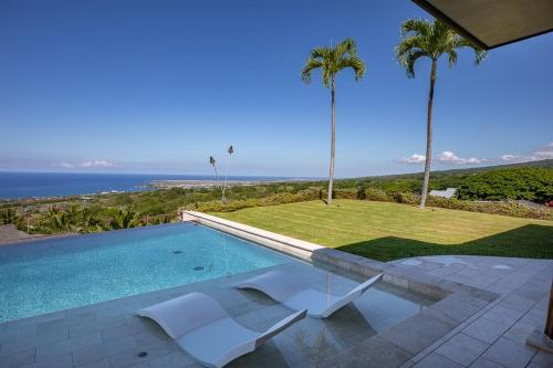 a swimming pool with two white chairs and palm trees at Hale La'i in Kailua-Kona