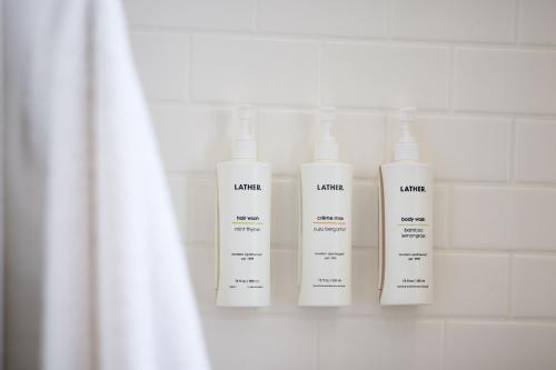 three white shampoo bottles are on a shelf in a bathroom at Archer Hotel Boston/Burlington in Burlington