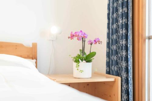 a vase with purple flowers on a table next to a bed at Chesa Michel in Bever