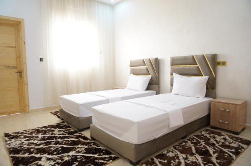 two beds in a bedroom with white sheets and a rug at 2 Voies Résidence in Dakhla