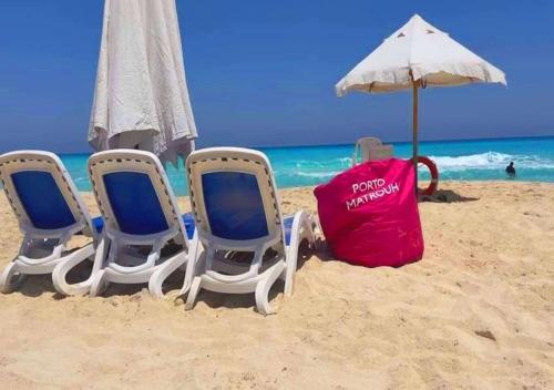 three chairs and an umbrella on a beach at شاليهات بورتو مطروح فيو بحر Porto Matrouh Sea View Families Only in Marsa Matruh
